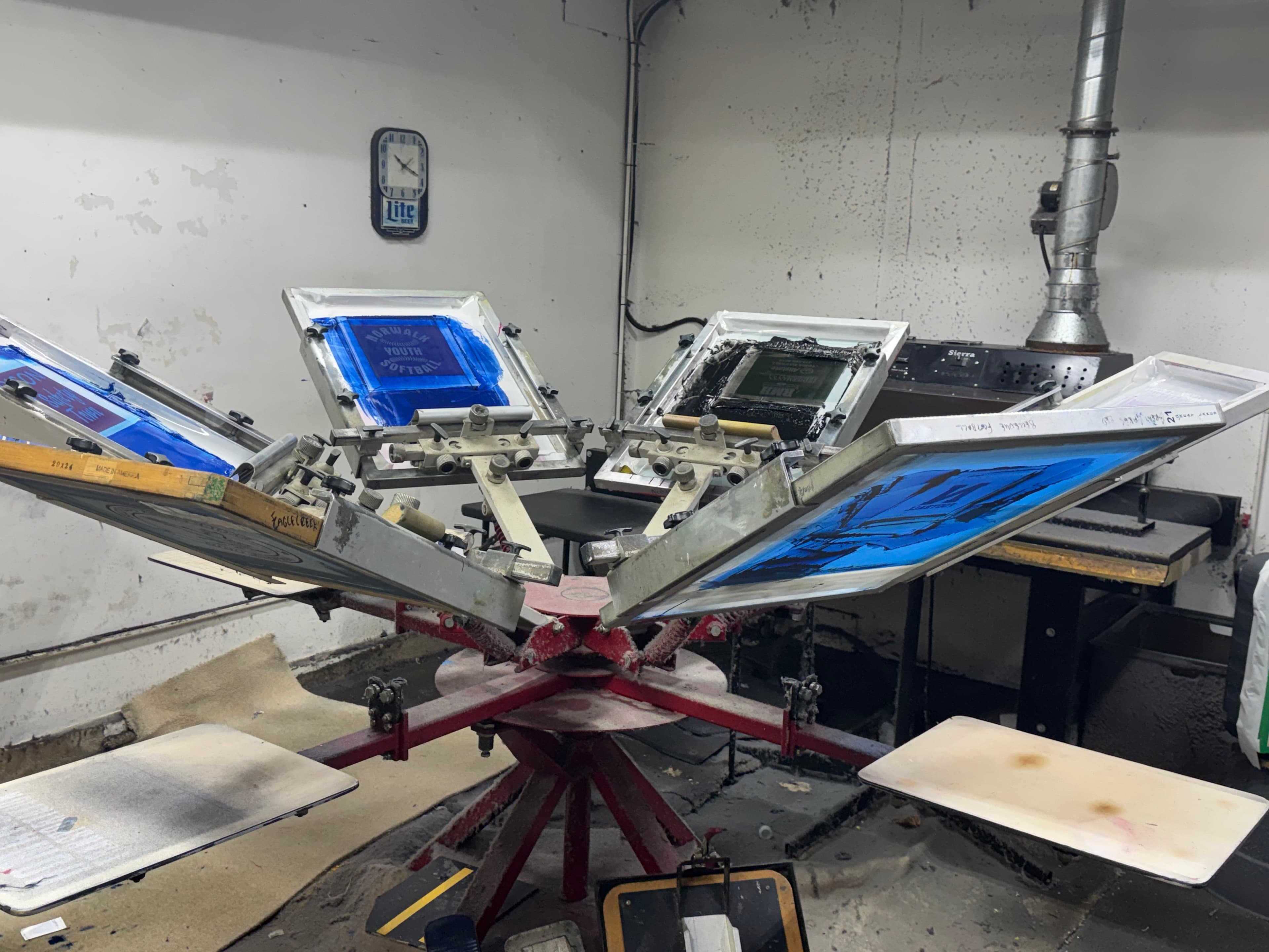 Industrial multi-station screen printing press with blue and black ink screens in a workshop.