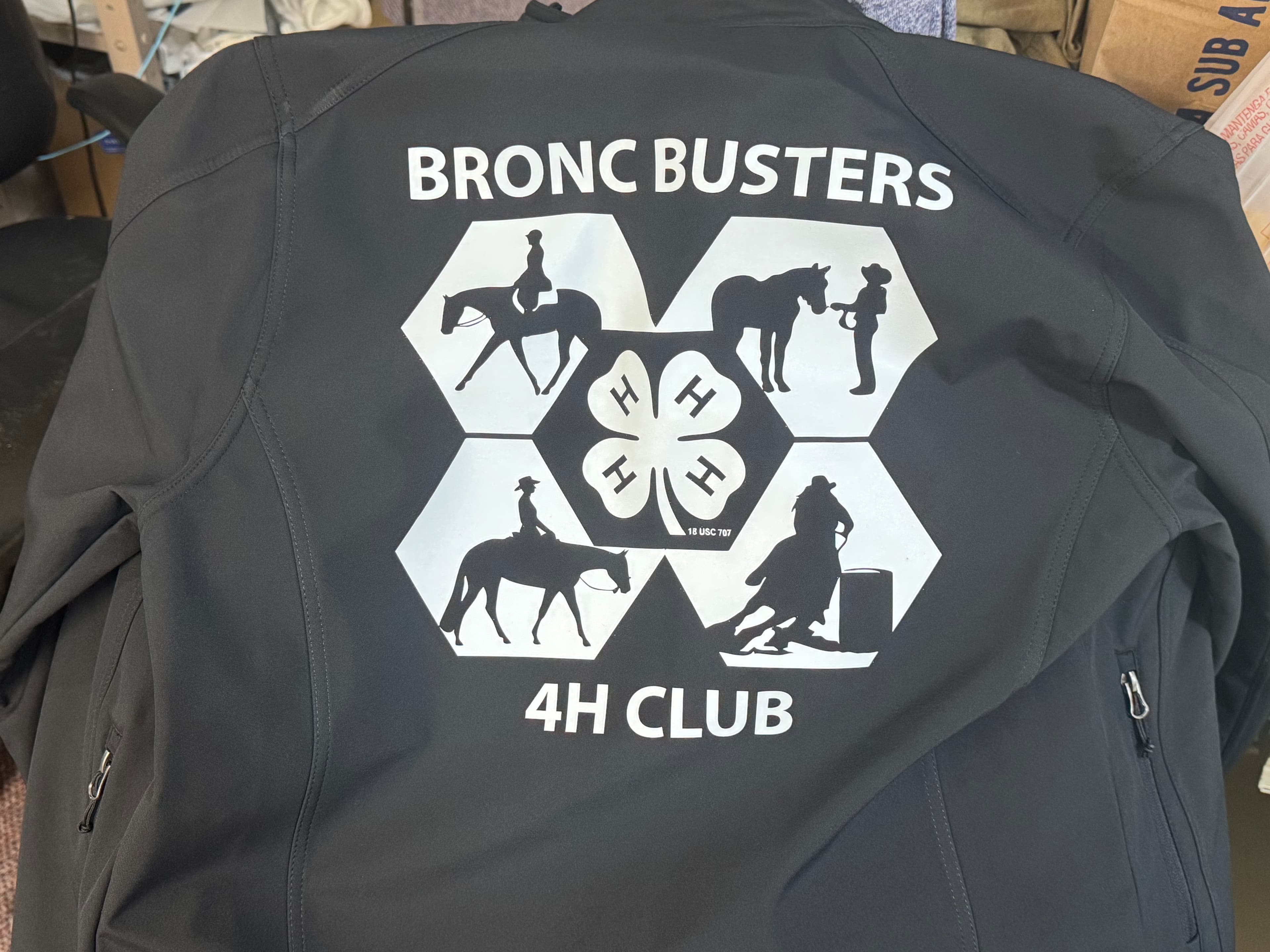 Black jacket back with BRONC BUSTERS 4H CLUB text and silhouettes of horse riding activities.